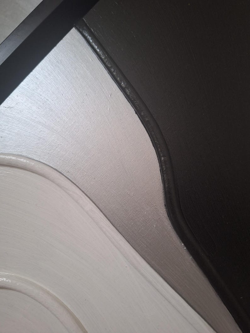 May include: Close-up of a painted surface with a curved design. The color scheme includes white, silver, gray, and black. The paint has a textured appearance, with visible brushstrokes.