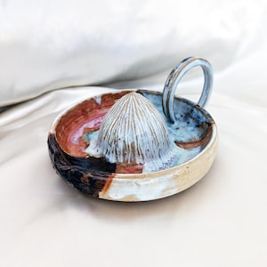 May include: A handmade ceramic citrus juicer with a light blue reamer and handle. The bowl features a mix of colors, including brown, blue, and pink. The juicer is designed for easy citrus fruit juicing.
