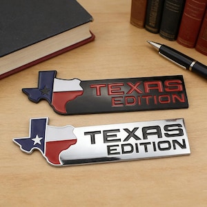 May include: Two car emblems with 'TEXAS EDITION' text. One is black with red text, the other chrome with black text. Both feature the Texas state outline in the state flag colours.
