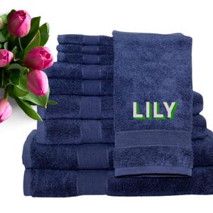 May include: A stack of navy blue bath towels and washcloths. One towel is embroidered with the name "LILY" in white and green. Pink tulips are in the upper left corner of the image.