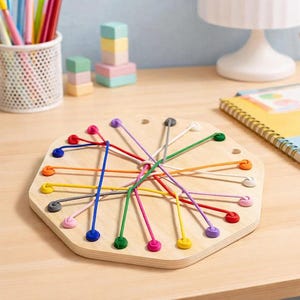 May include: Wooden lacing toy with a light wood finish. The toy features a hexagonal shape with colourful strings and pegs. The strings are in various colours, including blue, green, and pink. The pegs are also in different colours.