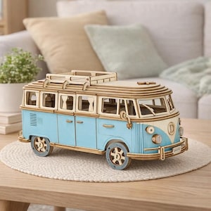 May include: A light blue and wood-coloured wooden model of a vintage van. The van has a detailed design with visible windows, wheels, and a roof rack. The model is placed on a light-coloured, round mat.