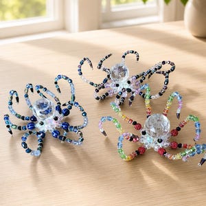 May include: Three octopus figurines crafted from faceted crystal beads and small glass beads. One features shades of blue, another displays a rainbow spectrum, and the third is composed of dark, iridescent beads, each with a central crystal sphere.