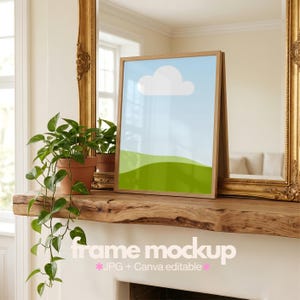 May include: A vertical wooden picture frame containing a minimalist graphic print of a light blue sky with a single white cloud above rolling green hills. The frame is positioned on a wooden mantelpiece next to a potted green trailing plant.
