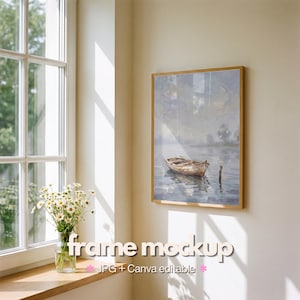 May include: A rectangular wooden frame containing a painting of a small boat on calm water, displayed on a light-colored wall. The text "frame mockup JPG + Canva editable" is overlaid at the bottom. A glass vase with white daisies sits nearby.