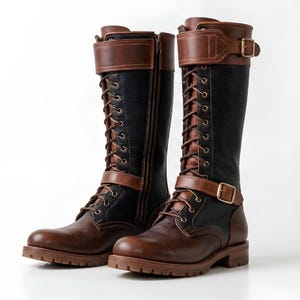 Puede incluir: Un par de botas hasta la rodilla que combinan paneles de cuero negro texturizado y cuero marrón liso. Estas botas incluyen cordones en la parte delantera, una cremallera lateral y dos correas de cuero marrón ajustables con hebillas de metal dorado.