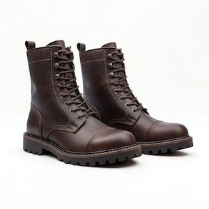 Op de afbeelding: Een paar donkerbruine leren veterschoenen met een neuskap, metalen oogjes, bijpassende bruine veters, een treklipje bij de hiel en een dikke, geprofileerde rubberen zool. De laarzen hebben zichtbare ton-sur-ton stiksels op de schacht en neus.