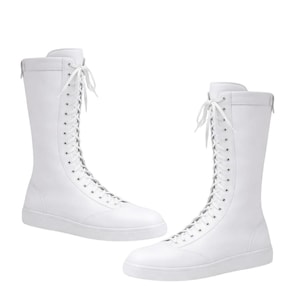 May include: A pair of tall, white lace-up boots featuring a smooth finish, a rounded toe, and a flat sole. The boots extend to the mid-calf and are secured with white laces threaded through silver-toned eyelets that run up the front center.