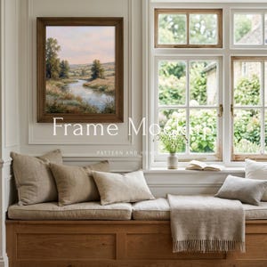 May include: A framed landscape painting with a river scene hangs above a wooden bench with beige cushions and pillows. The text "Frame Mockup" is visible. A window with a view of greenery is to the right.