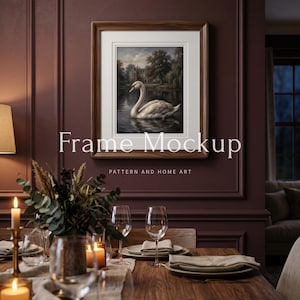 May include: A framed artwork featuring a swan on a lake, displayed above a dining table. The frame is brown, and the artwork has a white border. The text "Frame Mockup" and "PATTERN AND HOME ART" are visible. The table is set with candles, glasses, and plates.