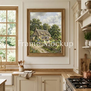 May include: A framed landscape painting of a cottage with a thatched roof, surrounded by lush greenery and a stone path. The frame is a warm, light brown color. The text "Frame Mockup" is displayed on the image.