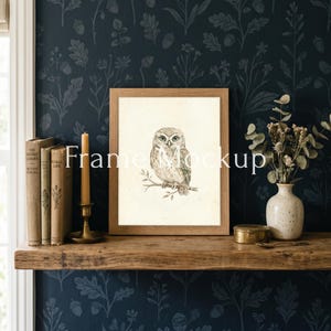May include: A framed owl print with the text "Frame Mockup" on a wooden shelf. The print is in a light brown wooden frame. The shelf also holds old books, a candle, and a small vase with dried flowers. The background is a dark blue floral wallpaper.