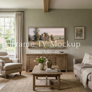 May include: A living room scene with a framed TV displaying a landscape painting. The room features a wooden coffee table, a beige sofa, and a matching armchair. A wooden cabinet and a rug complete the cozy, neutral-toned decor.