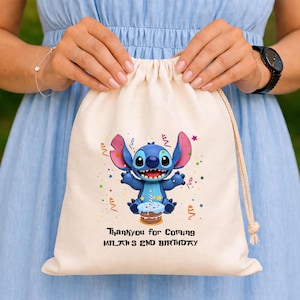 May include: A beige drawstring bag featuring a blue cartoon character with large ears, holding a cupcake. The bag has the text "Thankyou for Coming MILAN'S 2ND BIRTHDAY" printed in black. Colorful confetti and stars surround the character.