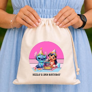 May include: A beige drawstring bag featuring a colorful graphic of Stitch and Lilo from the Disney movie Lilo & Stitch, celebrating a birthday. The graphic includes a birthday cake and the text "NEELU'S 3RD BIRTHDAY".