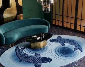 Puede incluir: Una alfombra ovalada con fondo azul claro que presenta dos peces koi de color azul oscuro nadando en ondas circulares. La alfombra está colocada sobre un suelo azul oscuro moteado frente a un sofá curvo color cerceta y una mesa de mármol negro.
