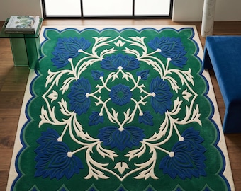 Puede incluir: Una alfombra rectangular con fondo verde intenso, borde festoneado y un patrón floral central simétrico en azul real y crema. El diseño consta de grandes flores azules similares a lotos conectadas por enredaderas de color crema.