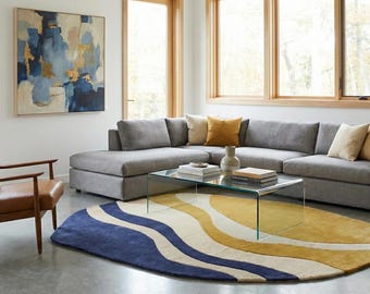 Puede incluir: Salón moderno con un sofá seccional gris, una mesa de centro de cristal y un sillón de cuero marrón. Una pintura abstracta colorida cuelga de la pared. Una alfombra con ondas azules, amarillas y blancas.