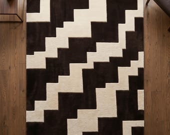 Peut inclure: Un tapis rectangulaire présentant un motif géométrique à fort contraste composé de blocs brun foncé et crème disposés selon un design en escalier ou en zigzag répétitif sur toute la surface du revêtement de sol.
