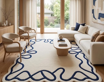 Puede incluir: Una alfombra rectangular grande con una base de color crema y un patrón de línea continua azul oscuro grueso que forma un borde ondulado y festoneado. La alfombra presenta una textura suave y afelpada sobre un suelo de madera clara.