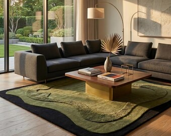 Puede incluir: Una alfombra grande con un diseño orgánico y ondulado en capas, en tonos verde oliva y negro. La alfombra está colocada sobre un suelo de madera clara bajo una mesa de centro cuadrada de madera con base dorada, con libros y un marco dorado encima.