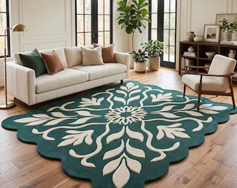 Puede incluir: Una alfombra grande de bordes festoneados con un fondo verde azulado profundo y un patrón floral simétrico de color crema que irradia desde el centro. La alfombra tiene una textura gruesa y afelpada sobre un suelo de madera.