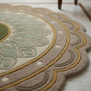 May include: A circular rug featuring a scalloped edge and a central medallion design. The rug displays a color palette of sage green, cream, mustard yellow, and taupe, with a tufted texture and small white dot accents along the outer border.
