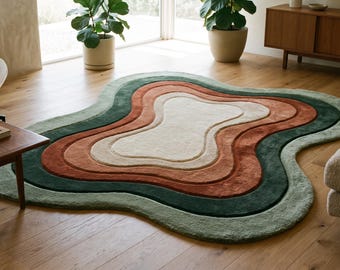 Puede incluir: Una alfombra de forma orgánica e irregular con capas concéntricas onduladas en tonos crema, terracota y verde bosque oscuro. La alfombra presenta una textura afelpada y copetuda con bordes elevados que definen cada sección.