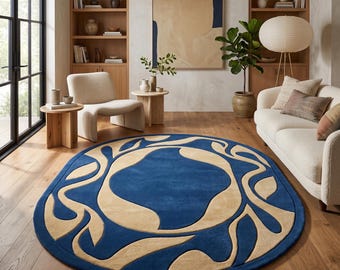 Puede incluir: Una alfombra ovalada grande que presenta un campo central de color azul intenso rodeado por un borde ancho de color beige con formas orgánicas, fluidas y similares a hojas que se extienden desde el centro hacia el borde.