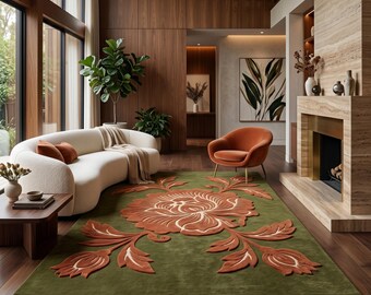 Puede incluir: Una alfombra rectangular con un fondo verde oliva intenso y un gran motivo floral central de pelo elevado en tonos naranja quemado y crema. El diseño incluye una flor central prominente con tallos de hojas simétricos.
