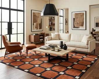 Puede incluir: Una sala de estar con una alfombra grande de patrón geométrico en naranja quemado, negro y crema. El espacio incluye un sofá color crema, un sillón de cuero marrón con su reposapiés a juego y una mesa de centro cuadrada de madera.