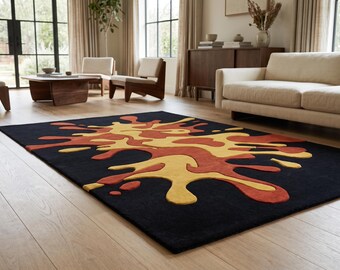 Puede incluir: Una alfombra rectangular con fondo negro y un gran patrón abstracto central de salpicaduras en tonos amarillo mostaza y naranja quemado. El diseño consta de formas orgánicas y fluidas que recuerdan a manchas de pintura líquida.