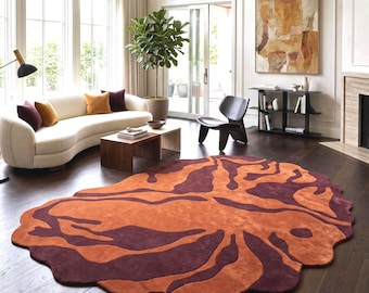 Puede incluir: Una alfombra de forma irregular con un patrón orgánico llamativo en tonos naranja quemado y granate oscuro. La alfombra tiene una textura suave y afelpada con un borde festoneado y asimétrico sobre un suelo de madera oscura.
