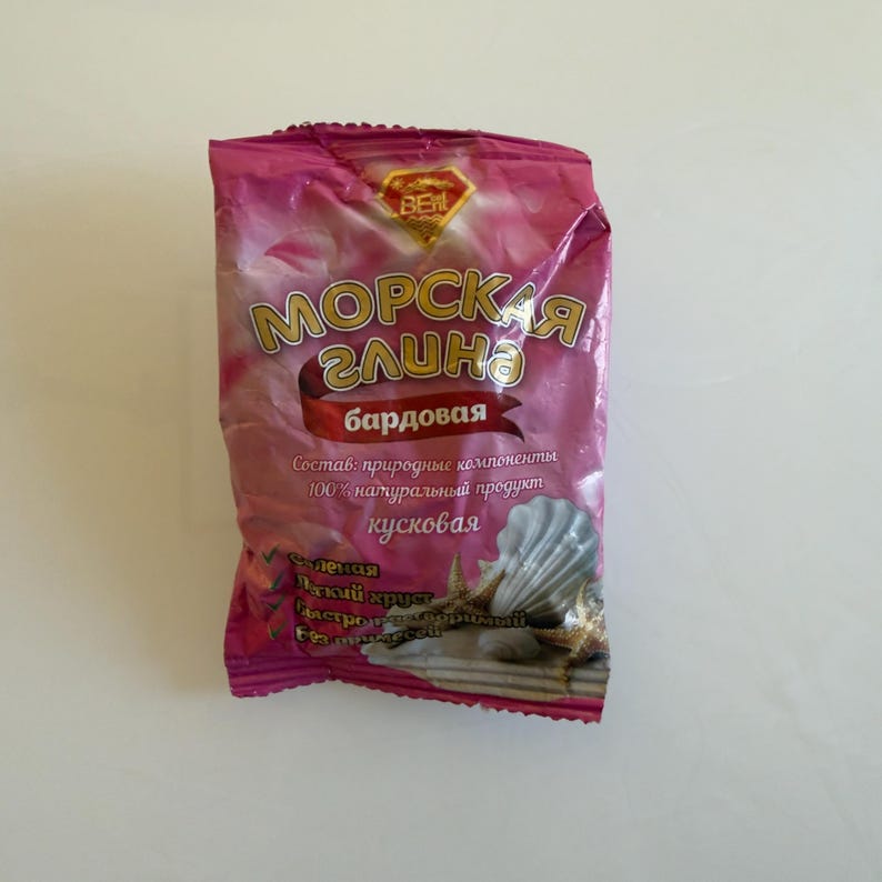 May include: A pink package of "Sea Clay" with Russian text. The package features gold lettering and a red banner with more text. The bottom of the package has a seashell and starfish design.