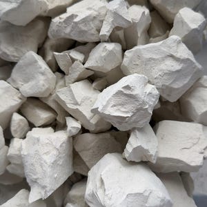 Puede incluir: Un montón de trozos de arcilla blanquecina de forma irregular. Las piezas varían en tamaño y tienen una superficie rugosa y texturizada. La imagen es un primer plano, que muestra los detalles del material natural.