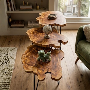 May include: A set of three wooden side tables with live edges and black metal legs. The tables are arranged in a tiered fashion, with a small globe, a compass, and a jade figurine displayed on top. The wood has a warm, natural grain.