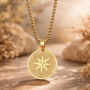May include: Gold-colored pendant necklace featuring a circular pendant with a sun design. The sun has a face and radiating lines. The chain and pendant are a matching gold color, creating a cohesive and elegant look. The necklace is displayed against a neutral background.