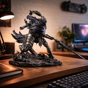 May include: A detailed, dark-toned figurine of a warrior in ornate armor, wielding a spear. The figure is posed dynamically on a textured base, with a flowing cape. The statue is set on a wooden desk, with a lamp and a keyboard in the background.