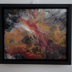May include: Abstract acrylic painting in a black frame. The artwork features a dynamic composition of swirling colors, including shades of red, orange, yellow, white, and black. The fluid paint creates a sense of movement and depth, suitable for home decor.