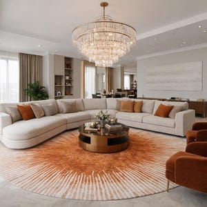 May include: A luxurious living room featuring a large, curved sectional sofa in a neutral color, complemented by orange accent pillows. A round, patterned rug in shades of orange and cream sits beneath a coffee table. Two orange armchairs and a crystal chandelier complete the elegant space.