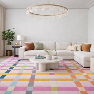 May include: A contemporary living room featuring a cream-colored corner sofa, a vibrant geometric rug, and a circular marble coffee table. A crystal chandelier illuminates the space. Cushions in shades of brown and green add a touch of color.