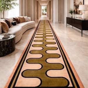 Puede incluir: Una alfombra de pasillo rectangular larga con un patrón de ondas verde oliva repetitivo centrado sobre un fondo color melocotón claro. El diseño está enmarcado por un borde negro grueso y un borde exterior fino color melocotón.