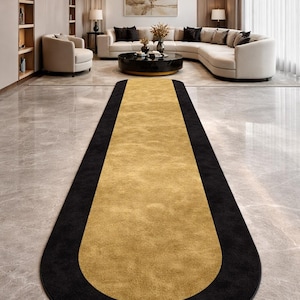 May include: A long, rectangular rug with a gold center and a black border. The rug is placed in a modern living room with a marble floor, a curved sofa, and a large chandelier.