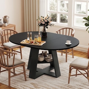 May include: A black oval dining table with a central pedestal base featuring an integrated storage shelf. The table is surrounded by four wooden chairs with light-colored seat cushions and spindle backs, arranged on a textured area rug.
