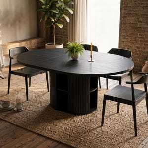 May include: A black oval dining table with a central fluted pedestal base featuring integrated open shelving. The table is accompanied by four matching black wooden chairs with curved backrests, a small green potted plant, and a single taper candle.
