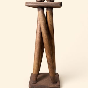 Peut inclure: Un support en bois brun foncé composé d'un plateau et d'une base carrés reliés par quatre pieds cylindriques entrecroisés. La structure est faite de bois teinté au grain visible, formant un cadre géométrique vertical au design stable.