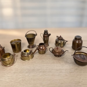 Könnte beinhalten: Eine Sammlung von Miniatur-Küchenutensilien aus Metall, darunter kleine Töpfe, Kessel, Eimer und Behälter. Diese winzigen Gefäße sind aus messing- und kupferfarbenem Metall gefertigt und weisen verschiedene Formen, Deckel und Griffe auf.