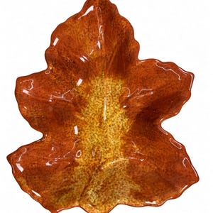 Puede incluir: Un plato de cerámica con forma de hoja de otoño grande y acabado brillante. El centro presenta un patrón moteado en amarillo y dorado que transiciona hacia tonos naranja quemado y marrón intenso en los bordes festoneados y texturizados.