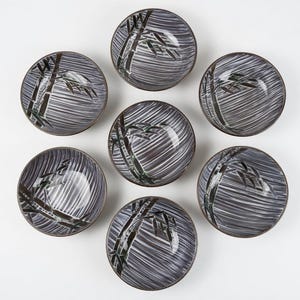 May include: Seven ceramic bowls with a gray and white striped pattern and a bamboo design. The bowls have a dark brown rim and are arranged in a circular pattern on a white background. The bowls are likely for serving food.