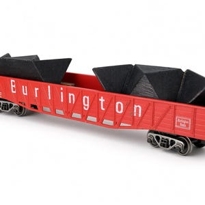 May include: A red model railway gondola wagon with the word Burlington printed in white on the side. The wagon features black metal wheels and is loaded with several angular black coal-like pieces. A small Burlington Route logo is visible.